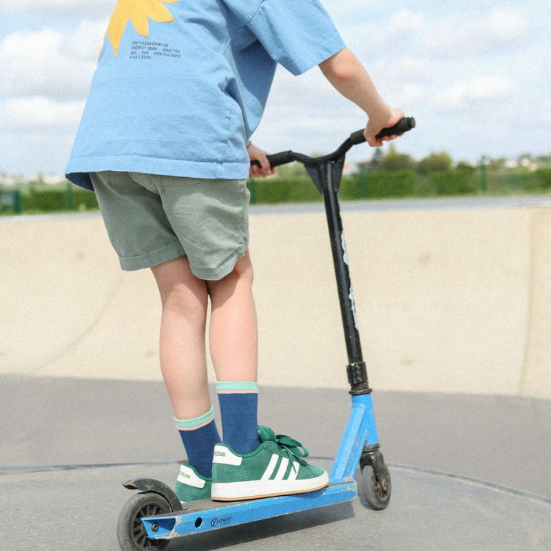 Chaussettes sans couture unies marine avec une bande verte portées dans un skateparc par un enfant sur une trotinette
