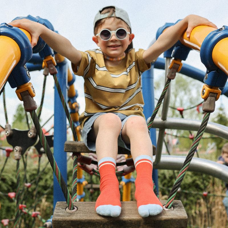 Chaussettes sans couture unies rouge avec une bande bleu ciel portées par un enfant dans un parc de jeux