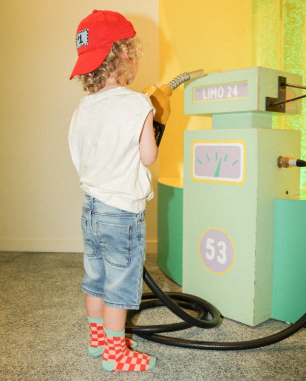 Photo des chaussettes à motifs enfant damier rouge et vert portées par un enfant dans une ambiance colorée.