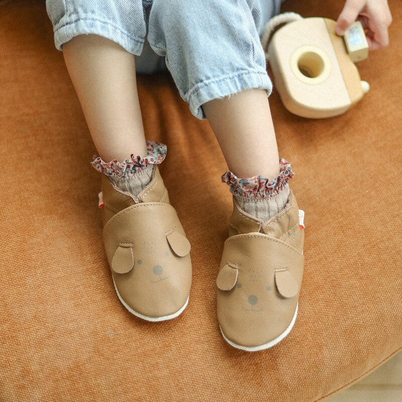 Chaussons en cuir souple marron motif tête de chien portés par un bébé