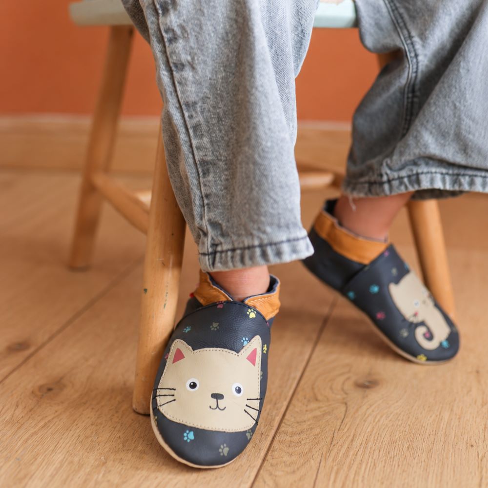 Photo des chaussons bebe cuir souple Nina le chat portés par une enfant sur un fond coloré.