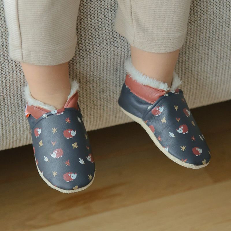 Chaussons cuir souple fourrés à motifs hérissons portés par un bébé.