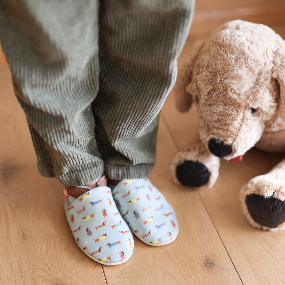 Photo des chaussons cuir souple Raphael les teckels portés par un enfant avec une peluche chien.