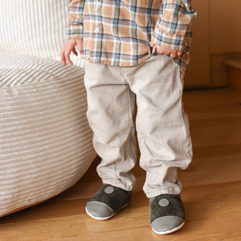 Chausson cuir souple fourre velours kaki portés par un enfant devant un pouf ans une ambiance hivernale.