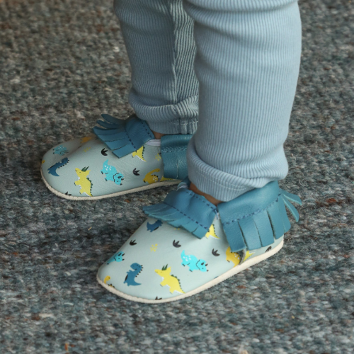 Photo des chaussons en cuir souple bébé à franges bleu nestor les dinosaures portés par un enfant.