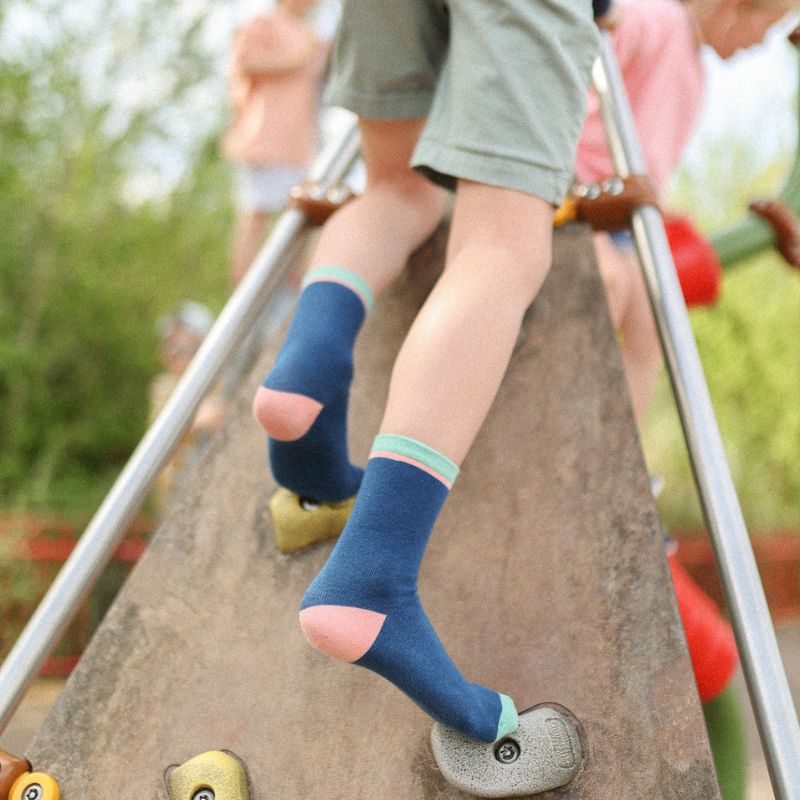 Chaussettes sans couture unies marine avec liserai vert portées par un enfant sur un mur d'escalade.
