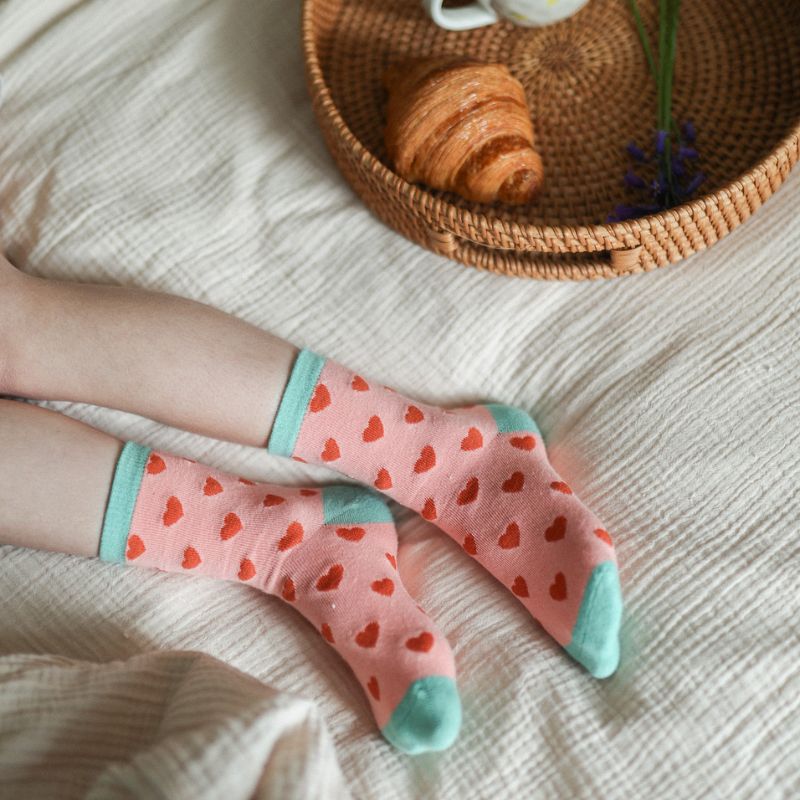 Chaussettes sans couture à motifs cœurs rouge portées par un enfant sur un drap de lit.