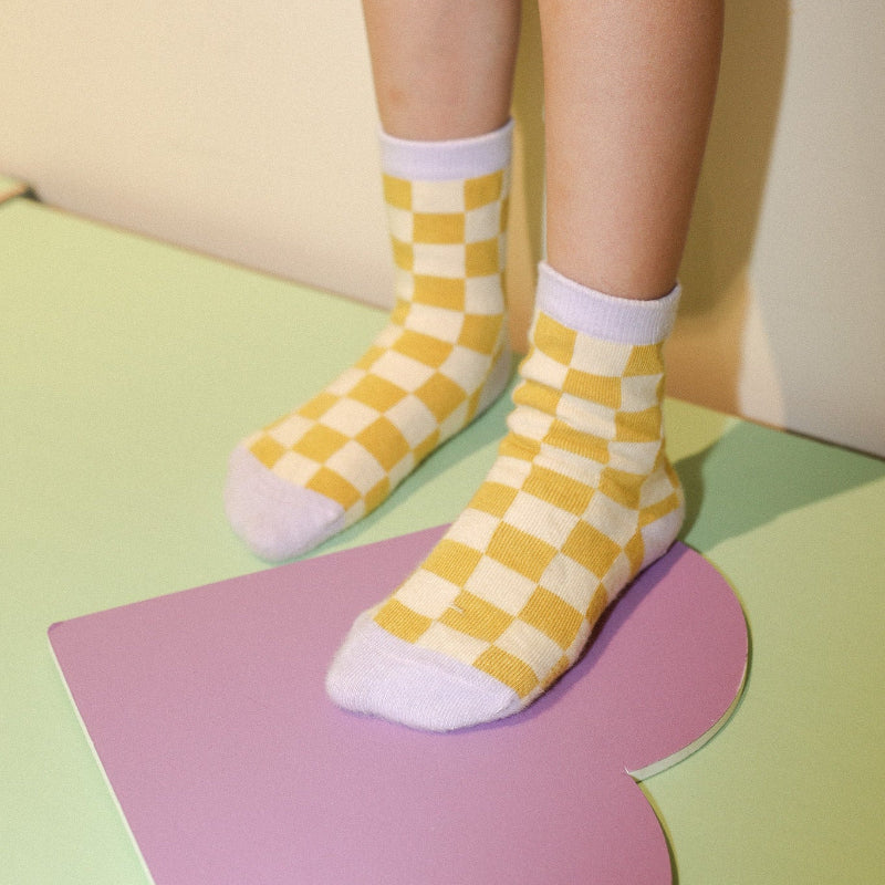 Chaussettes sas couture damier ocre et violet portées par une petite fille.