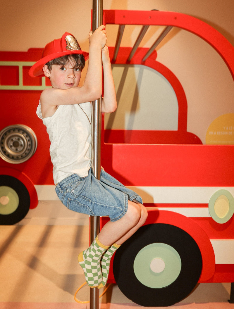 Chaussettes sans couture damier vert olive et ocre portées par un enfant dans une ambiance pompiers.