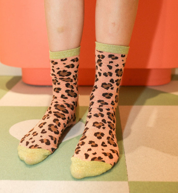 chaussettes sans couture enfant léopard à paillettes vert et rose portées par un enfant debout.