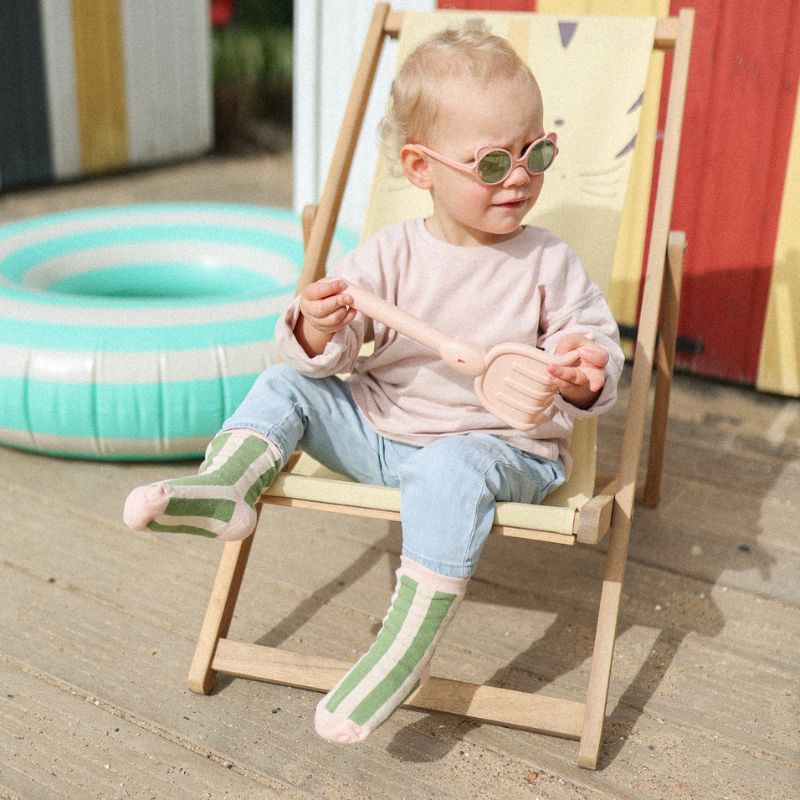 Chaussettes sans coutures rayées vert et et rose portées par un bébé sur une chaise longue de plage