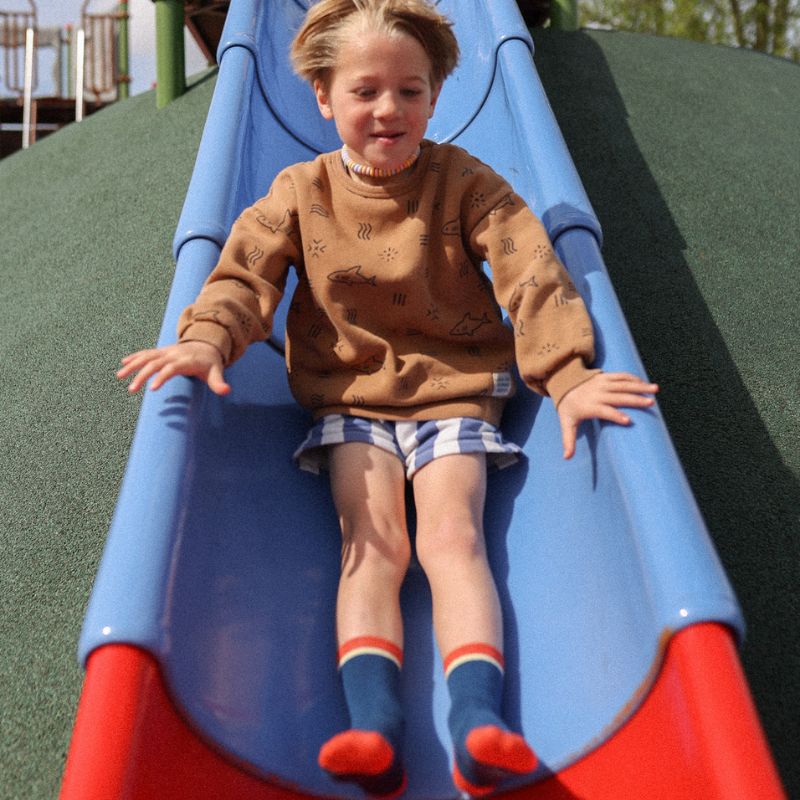 Chaussettes sans couture unies marine et rouge portée par un enfant glissant sur un toboggan.