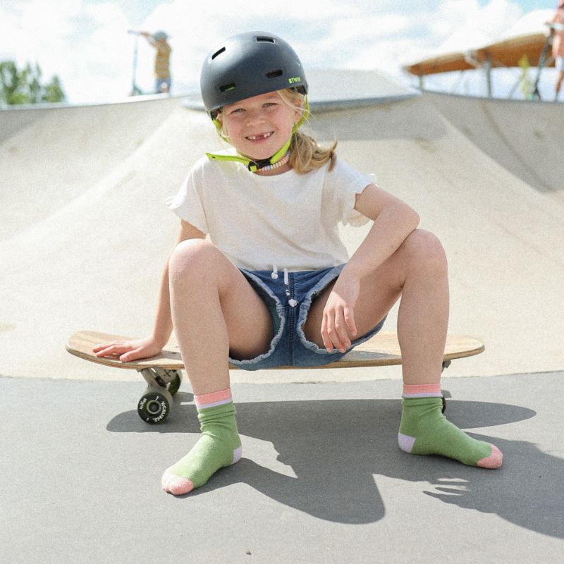 Chaussettes sans coutres unies vert olive avec bande rose portées par une enfant sur un skate