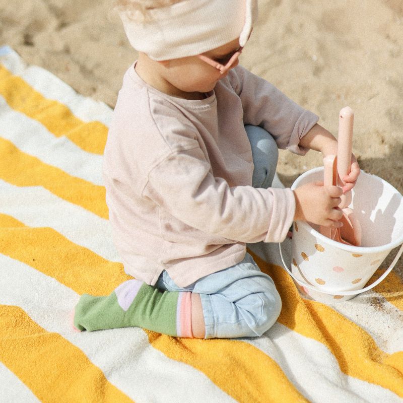 Chaussettes sans coutres unies vert olive avec bande rose portées par un bébé assis sur une serviette de plage