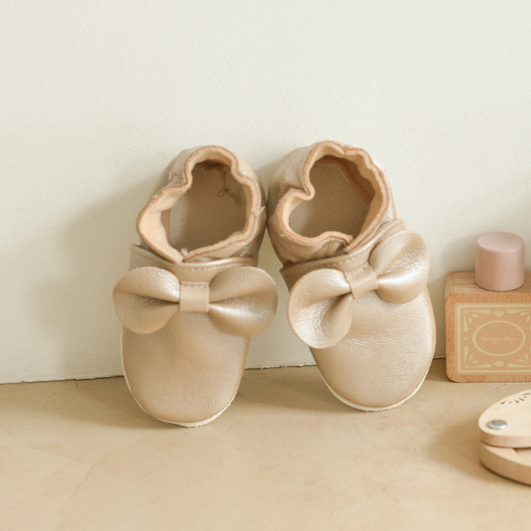 Photo des chaussons en cuir souple bébé Noeuds beige mis en ambiance feutré et poudré.