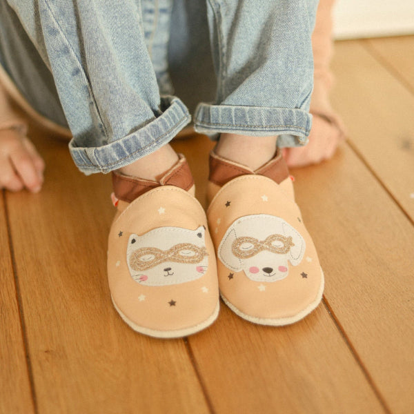 chaussons cuir souple rose avec imprimés chat et chien portés par un enfant.