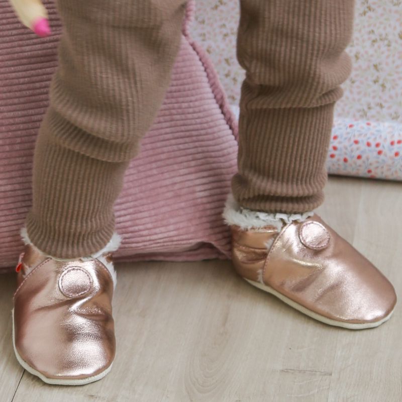 Chaussons cuir souple unis rose métalliques fourrés portés par un bébé.