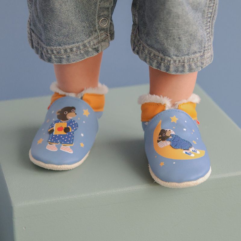 Chaussons fourrés en cuir souple coloris bleu et imprimés Petit Ours Brun portés par un bébé
