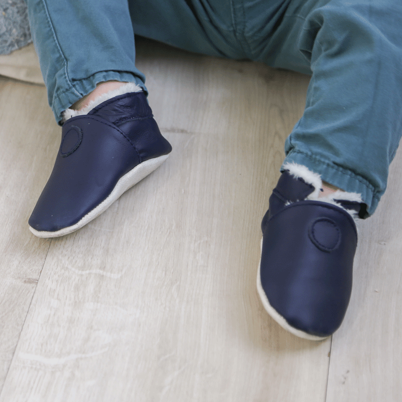 Chaussons fourrés en cuir souple de couleur bleu marine portés par un bébé