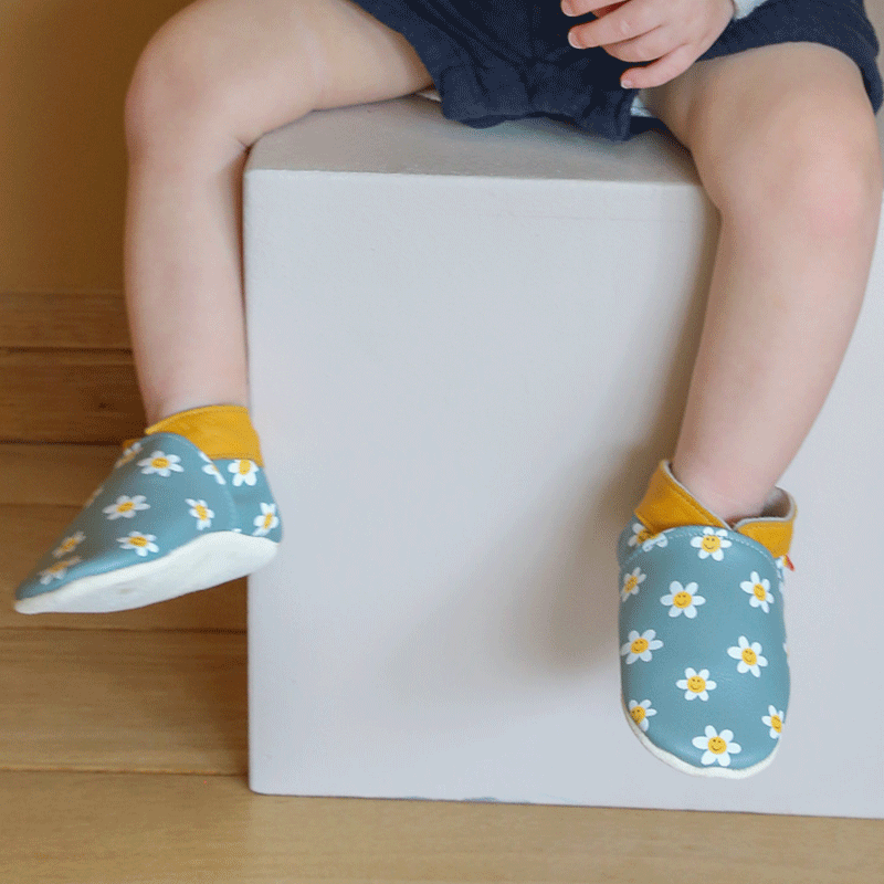 Chaussons en cuir souple et à motifs pâquerettes portés par un enfant 
