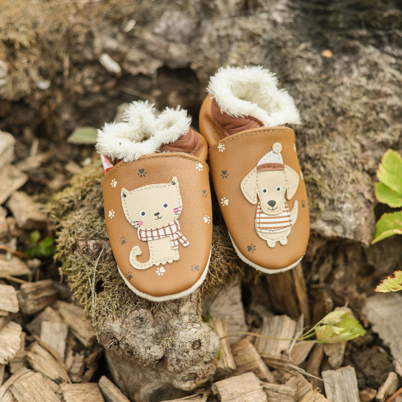 chaussons cuir souple bébé fourré Come et Claire en forêt sur fond d'écorces de bois